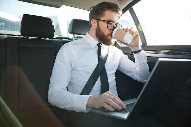 Hombre de negocios barbudo usando laptop y tomando café