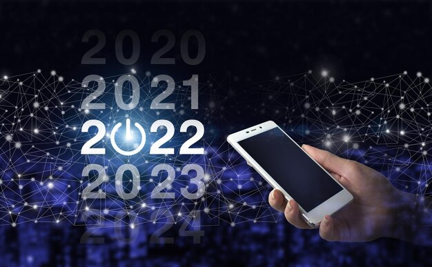 Hombre de negocios bienvenido año 2022. Asimiento de la mano smartphone blanco con holograma digital 2022 firmar sobre fondo borroso oscuro de la ciudad. Año de carga 2021 a 2022. Concepto de inicio.