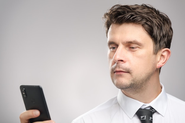 Hombre de negocios con camisa blanca y corbata mirando en su teléfono inteligente, para leer mensajes en el correo. Trabajador corporativo planificación de reuniones en su calendario en un teléfono inteligente.