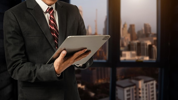 Hombre de negocios con camisa blanca que usa o navega por Internet en una tableta digital con un fondo borroso de ciudad de oficina modernaxA