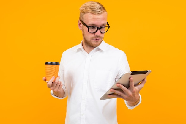 Hombre de negocios con una camisa blanca con una tableta y una taza de café en la mano sobre un fondo amarillo con espacio de copia.