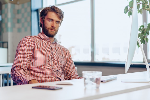 Hombre de negocios cansado que trabaja en su computadora en oficina de espacio abierto. Fin de la jornada laboral.