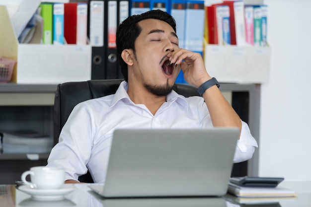 Hombre de negocios cansado usando laptop y bostezando