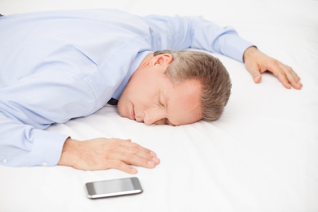 Hombre de negocios cansado. Vista superior del hombre cansado de cabello gris con camisa azul durmiendo en la cama