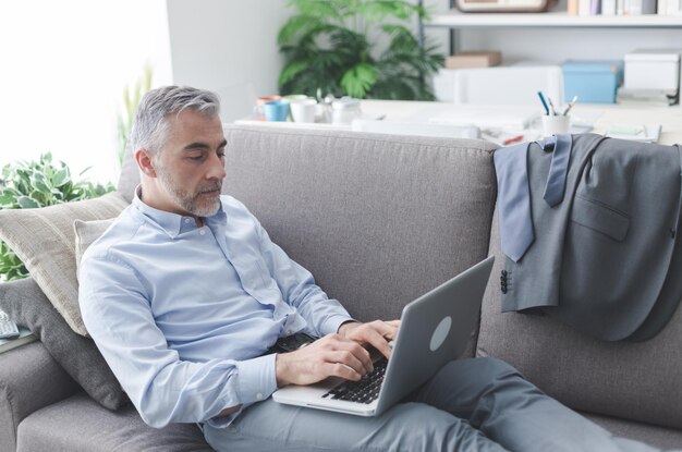 Hombre de negocios en casa está acostado y trabajando desde el concepto de negocio y estilo de vida del sofá