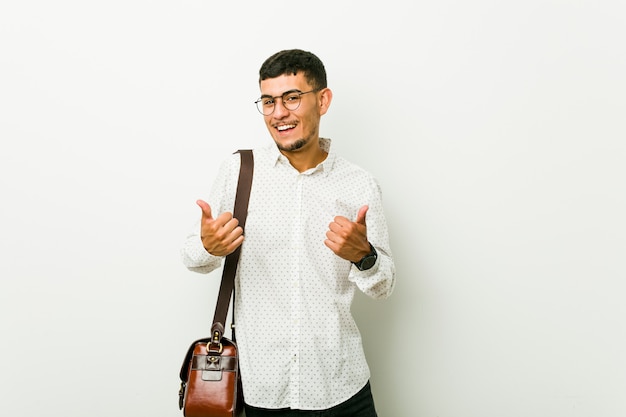 Hombre de negocios casual hispano joven levantando ambos pulgares, sonriente y confiado.