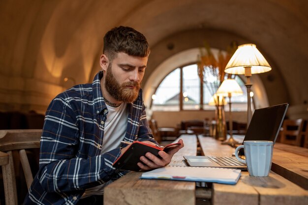 Hombre de negocios casual o autónomo que planifica su trabajo en el cuaderno que trabaja en la computadora portátil con smar ...