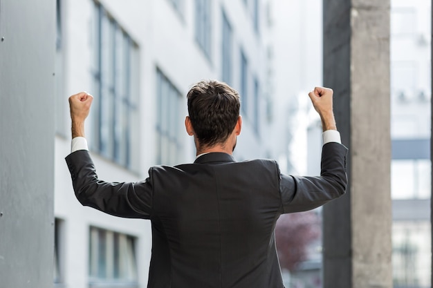 Hombre de negocios caucásico acertado con los brazos arriba celebrando la victoria. Concepto: éxito, crecimiento profesional, victoria, libertad. Empleado de hombre de negocios de silueta en el fondo de un edificio de oficinas moderno. fuera de