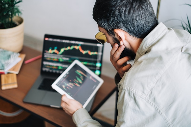 Hombre de negocios caucásico comerciando en línea, utilizando tecnología informática, mirando el comercio bursátil y analizando