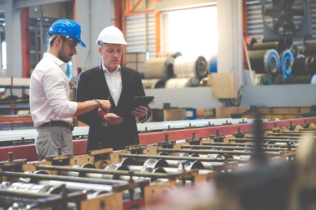 Hombre de negocios caucásico e ingeniero de fábrica hablando y discutiendo en el trabajador de la fábrica de fabricación de la industria pesada en casco de seguridad en las instalaciones industriales de la fábrica