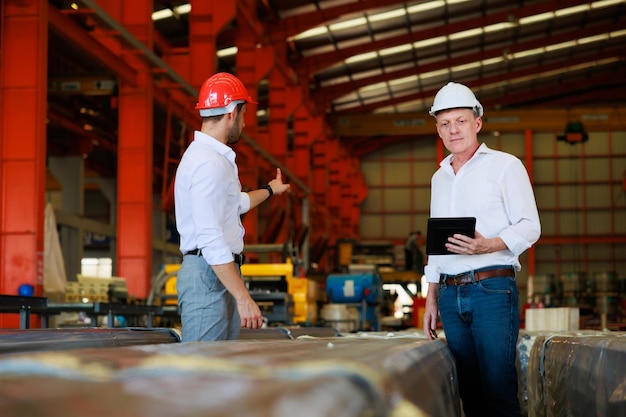 Hombre de negocios caucásico e ingeniero de fábrica hablando y discutiendo en el trabajador de la fábrica de fabricación de la industria pesada en casco de seguridad en las instalaciones industriales de la fábrica