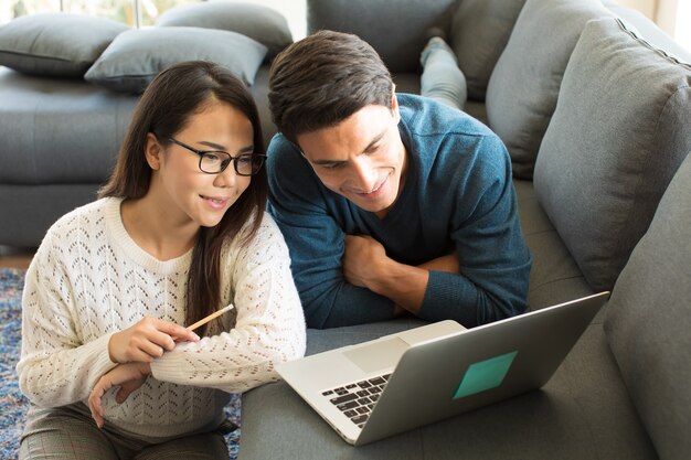 Hombre de negocios caucásico y empresaria asiática con vestido casual sentados juntos en la sala de estar y trabajando en equipo portátil con relax y felicidad. Idea para el trabajo moderno en casa.