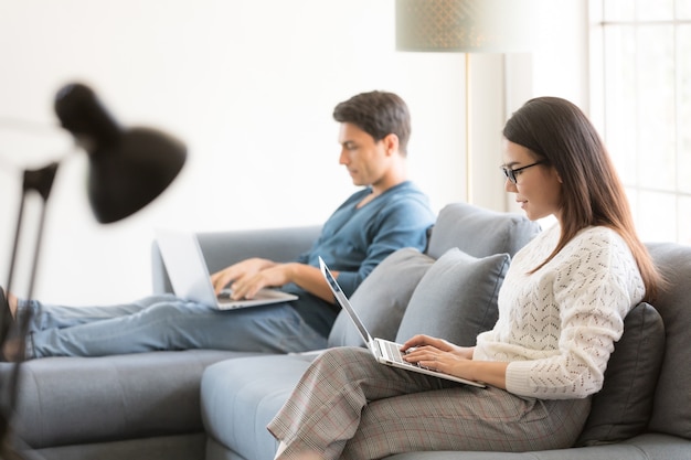 Hombre de negocios caucásico y empresaria asiática con vestido casual sentados juntos en la sala de estar y trabajando en equipo portátil con relax y felicidad. Idea para el trabajo moderno en casa.