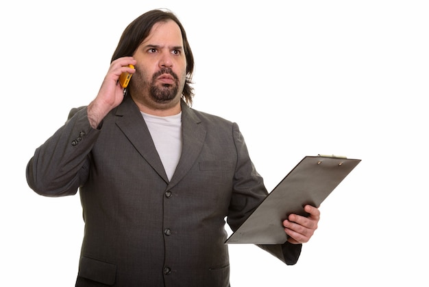 Hombre de negocios caucásico gordo sorprendido hablando por teléfono y sosteniendo el portapapeles mientras piensa