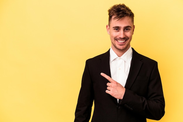 Hombre de negocios caucásico joven aislado sobre fondo amarillo sonriendo y apuntando a un lado, mostrando algo en el espacio en blanco.