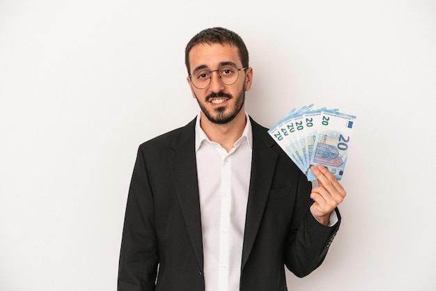 Hombre de negocios caucásico joven con billetes aislados sobre fondo blanco feliz, sonriente y alegre.