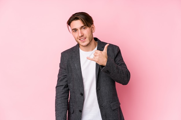 Hombre de negocios caucásico joven posando mostrando un gesto de llamada de teléfono móvil con los dedos.