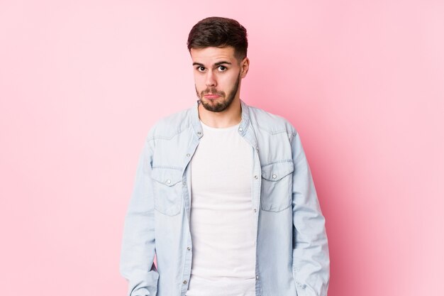 El hombre de negocios caucásico joven que presenta en un blanco aislado se encoge de hombros y abre los ojos confundidos.