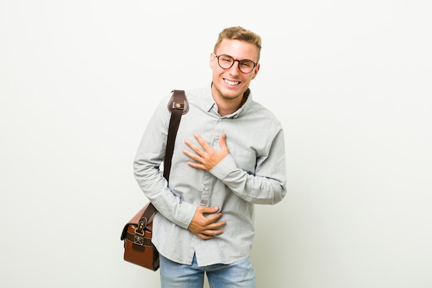 Hombre de negocios caucásico joven se ríe felizmente y se divierte manteniendo las manos en el estómago.