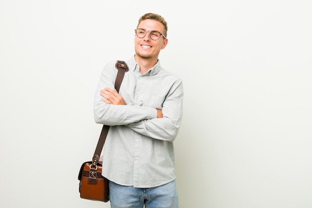 Hombre de negocios caucásico joven sonriendo confiado con los brazos cruzados.