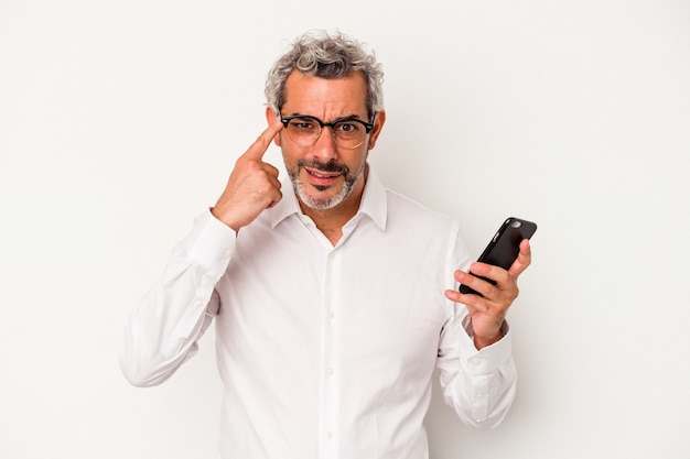 Hombre de negocios caucásico de mediana edad sosteniendo un teléfono móvil aislado sobre fondo blanco mostrando un gesto de decepción con el dedo índice.