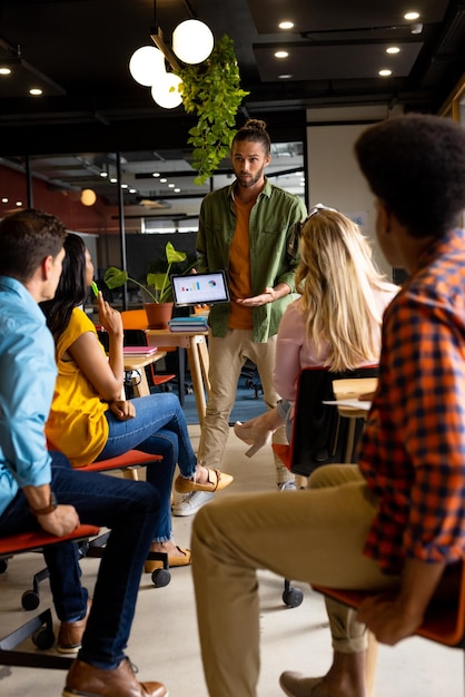 Foto un hombre de negocios caucásico que presenta a varios colegas usando una tableta en la oficina. oficina casual, negocios, presentación, trabajo en equipo y trabajo creativo, inalterado.