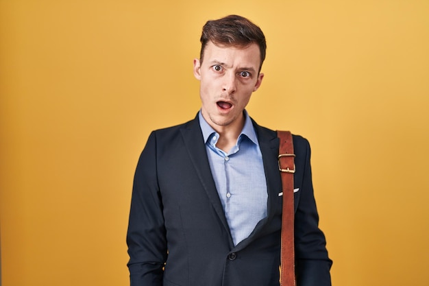 Hombre de negocios caucásico sobre fondo amarillo con cara de shock, luciendo escéptico y sarcástico, sorprendido con la boca abierta