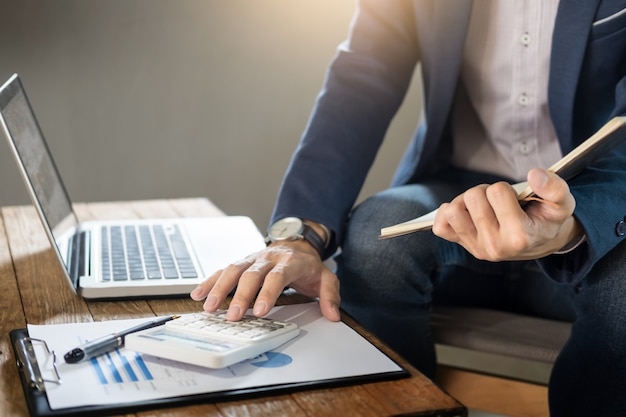 Hombre de negocios la celebración de un bloc de notas en blanco y calcular el negocio de negocio de beneficios de negocios con calculadora en cafetería o café con un ordenador portátil