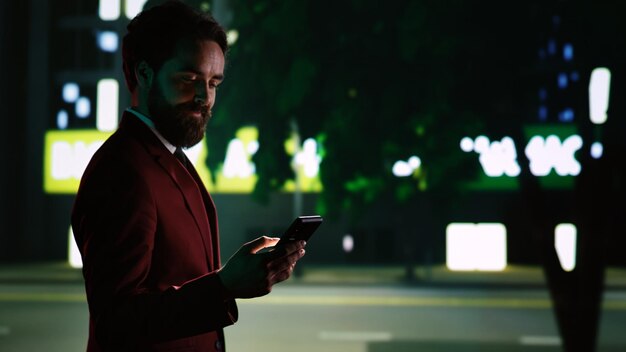 Hombre de negocios de clase revisa mensajes en una caminata nocturna, paseando por el distrito del centro y buscando direcciones en la acera. Hombre confiado caminando por la ciudad, paseo nocturno. Disparo de mano.