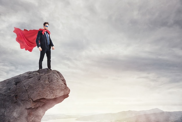 Hombre de negocios como un superhéroe en la cima de una montaña