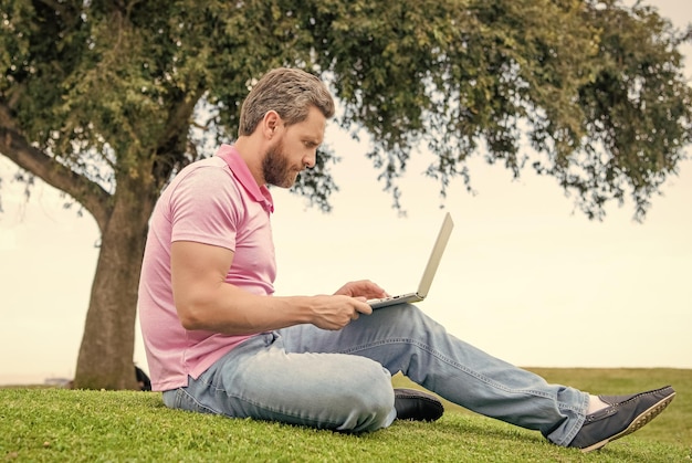 Hombre de negocios concentrado que usa una computadora portátil para bloguear sobre el trabajo de hierba verde en línea