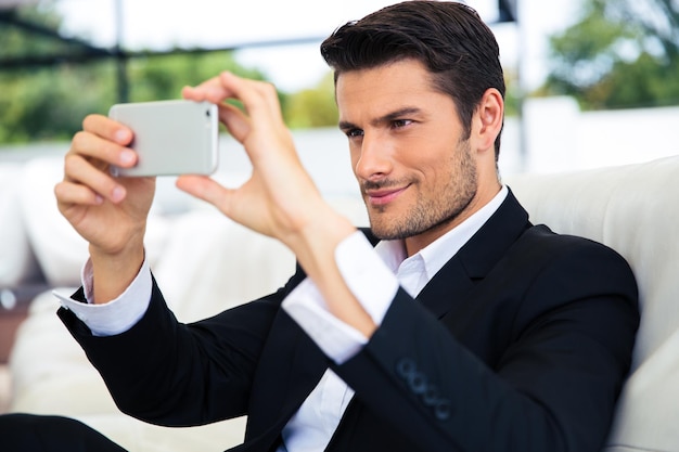 Hombre de negocios confiado que hace la foto del selfie en el teléfono inteligente en el restaurante