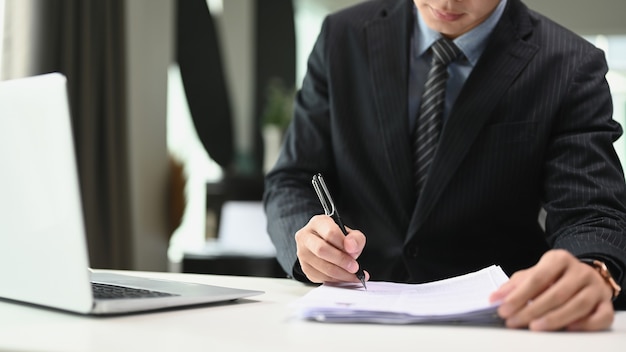 Un hombre de negocios confiado en traje negro está escribiendo notas o informe financiero en la oficina moderna.