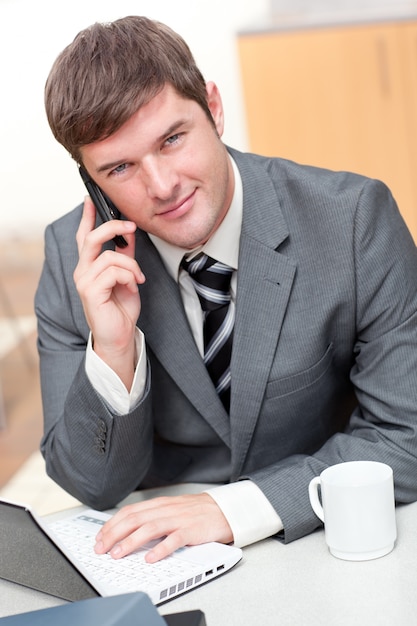 Hombre de negocios confidente que habla en el teléfono y que usa su computadora portátil