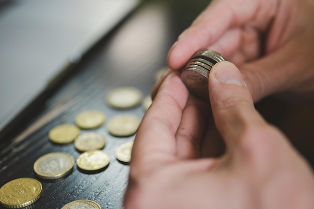 Hombre de negocios contando dinero. Las manos masculinas ricas sostiene y cuentan monedas de diferentes euros en la mesa delante de un portátil.