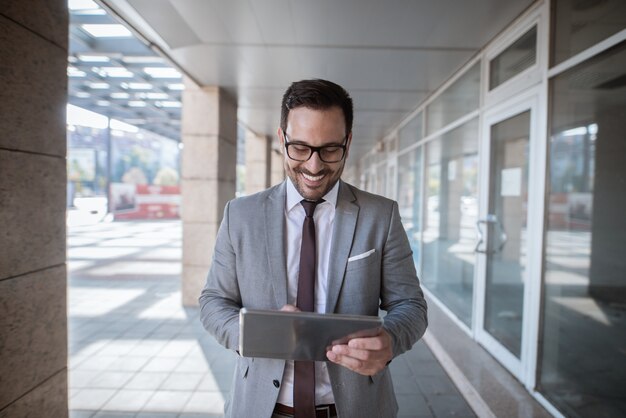 Hombre de negocios corporativo que usa la tableta para comprobar el correo electrónico mientras está de pie delante del escaparate Cintura para arriba retrato.