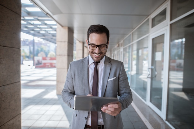 Hombre de negocios corporativo que usa la tableta para comprobar el correo electrónico mientras está de pie delante del escaparate cintura para arriba retrato.