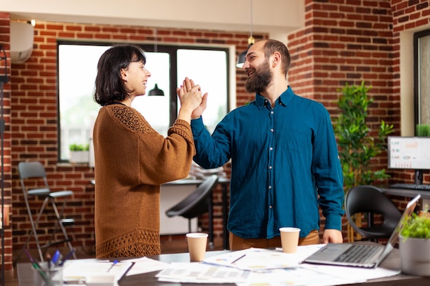 Hombre de negocios dando cinco a la mujer gerente después de finalizar el proyecto empresarial trabajando en la presentación de marketing en la oficina de inicio. Empresarios analizando la reunión de empresa de planificación de estrategia de gestión