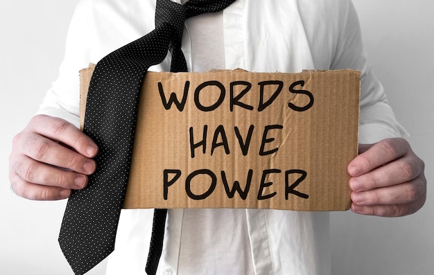 Un hombre de negocios desaliñado sostiene un cartel de cartón con las palabras Words Have Power