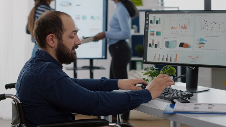 Foto hombre de negocios discapacitado discapacitado en silla de ruedas discutiendo con un colega, pidiendo información escribiendo en la computadora, verificando datos estadísticos que trabajan en la puesta en marcha de una oficina comercial con un equipo diverso