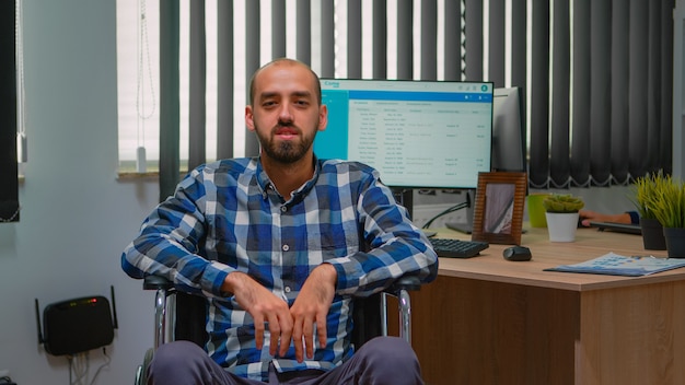 Hombre de negocios discapacitado discapacitado en silla de ruedas saludando en videollamada con conferencia en línea en la oficina de negocios. Trabajador autónomo paralizado e inmovilizado que trabaja en una empresa financiera con tecnología moderna.