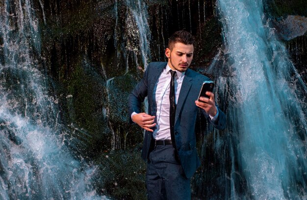 Hombre de negocios con dispositivo en teletrabajo hombre de negocios en traje sosteniendo una computadora portátil en la cascada al aire libre