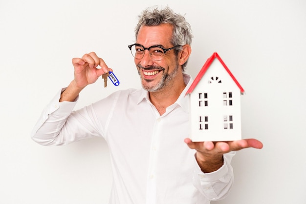 Hombre de negocios de edad ociosa sosteniendo llaves y casa de juguetes aislada en el fondo azul