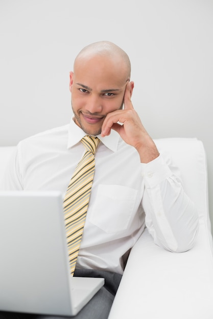 Hombre de negocios elegante con la computadora portátil que se sienta en el sofá en casa