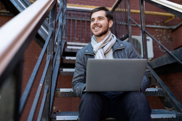 Hombre de negocios elegante con una computadora portátil de rodillas sentado en las escaleras en el emprendimiento de la oficina