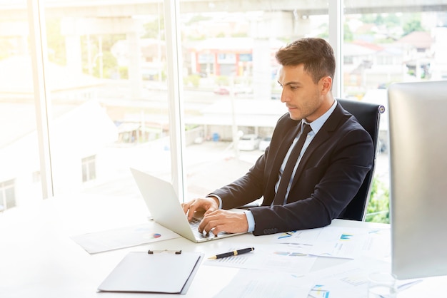 Hombre de negocios elegante joven que trabaja con el ordenador portátil en el escritorio en oficina moderna.