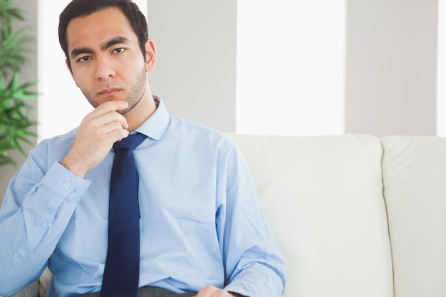 Hombre de negocios elegante pensativo que se sienta en el sofá acogedor