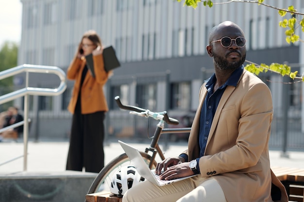 Un hombre de negocios elegante con ropa formal y gafas de sol escribiendo en el teclado de una computadora portátil