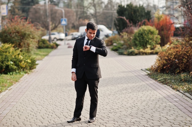 Hombre de negocios elegante del sur de Asia en traje mirando sus relojes inteligentes en la mano.