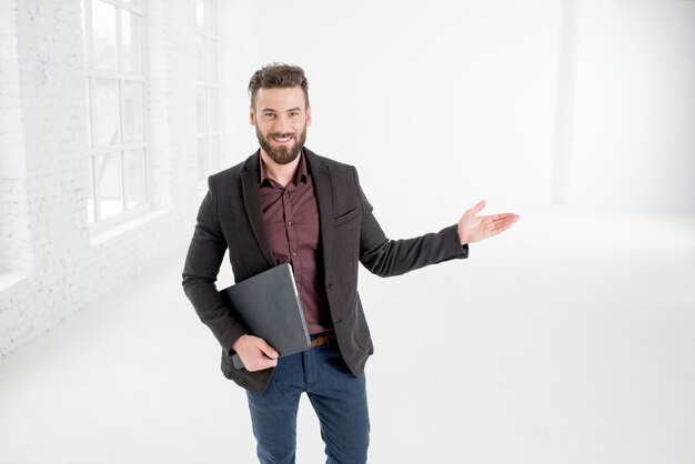 Hombre de negocios elegante en el traje oscuro que muestra con la mano que se coloca en el interior de la oficina blanca